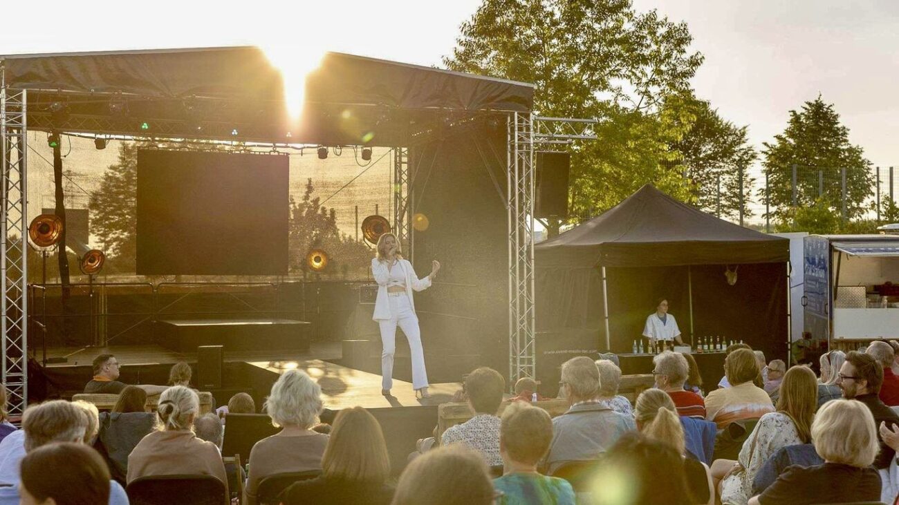 Helene Fischer Double Caro tritt bei einer Open-Air-Show auf einer Bühne vor Publikum auf, Sonnenuntergang, professionelle Lichttechnik, Konzertbesucher erleben Live-Musik in sommerlicher Atmosphäre.
